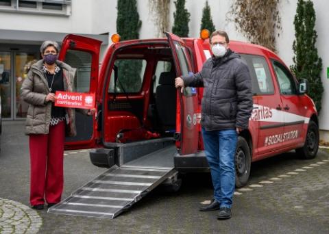 Foto des Fahrzeugs der Caritas mit ausgefahrener Rampe. Zwei Mitarbeiter stehen dabei und tragen eine Maske